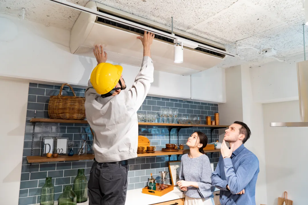 A repairman wearing a yellow helmet and checking the air conditioner