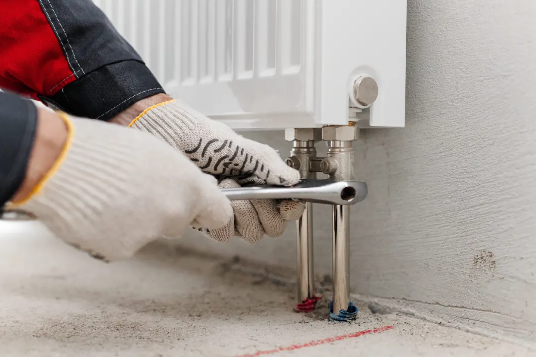 Hands Using Wrench To Tighten Radiator Valves During Installation. Plumbing Work In Unfinished Interior Space.